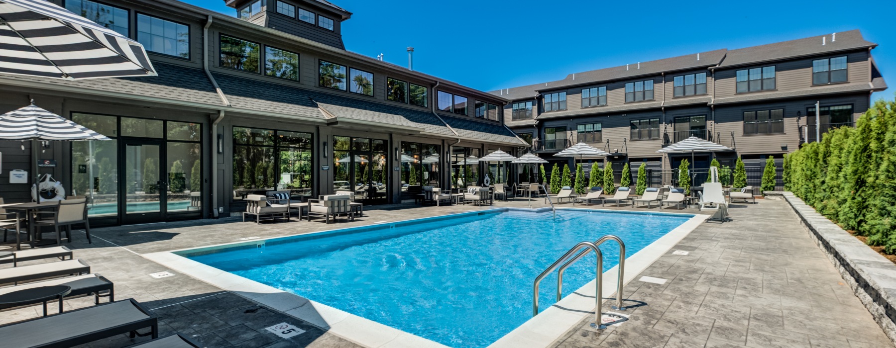 Bright, sparkling resort-style outdoor swimming pool surrounded by luxury lounge chairs and modern apartment buildings at Brookside Wilton in CT