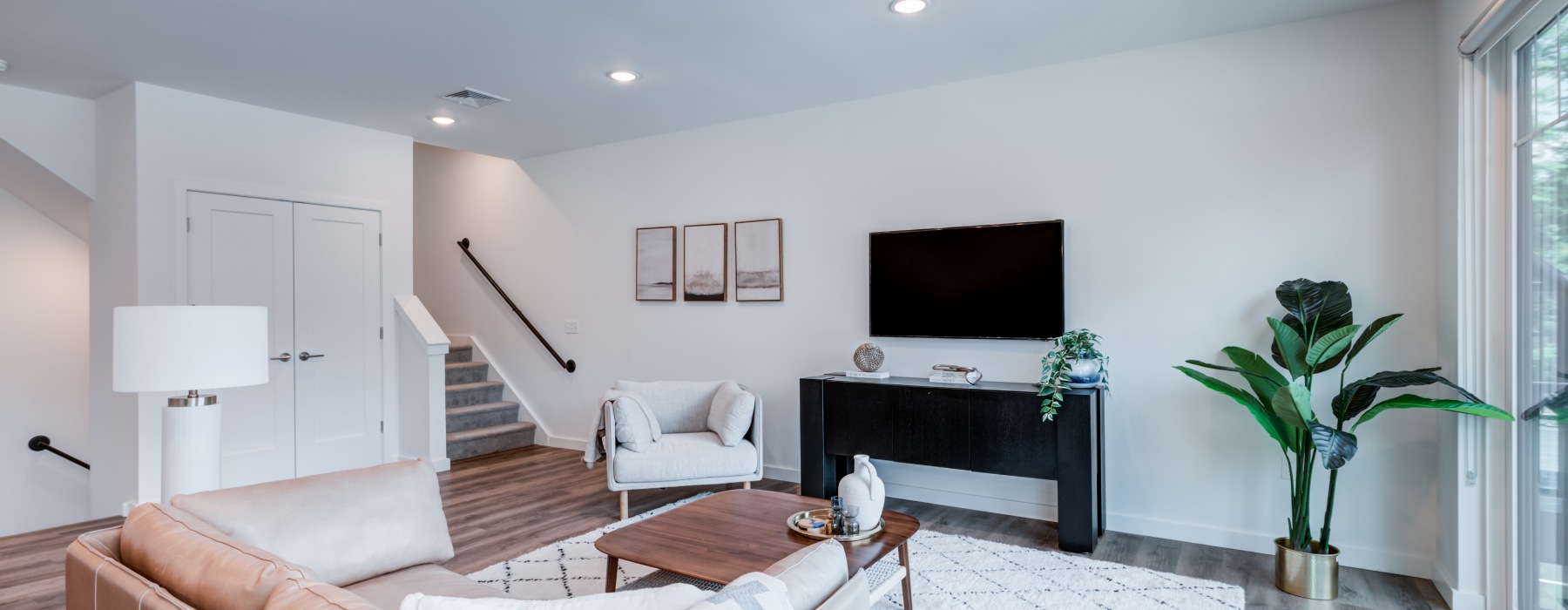 Bright modern model apartment living room with stylish furniture, a flat-screen TV, and staircase at Brookside Wilton in CT