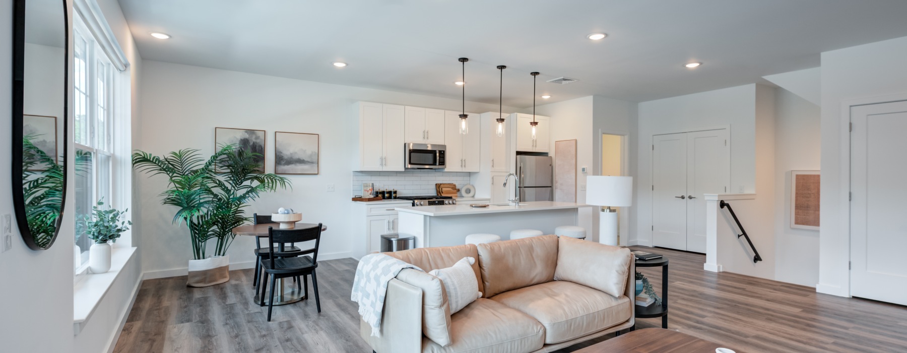 Open-concept model apartment living room with a modern grey sofa, hardwood floors, and a view into the kitchen at Brookside Wilton in CT