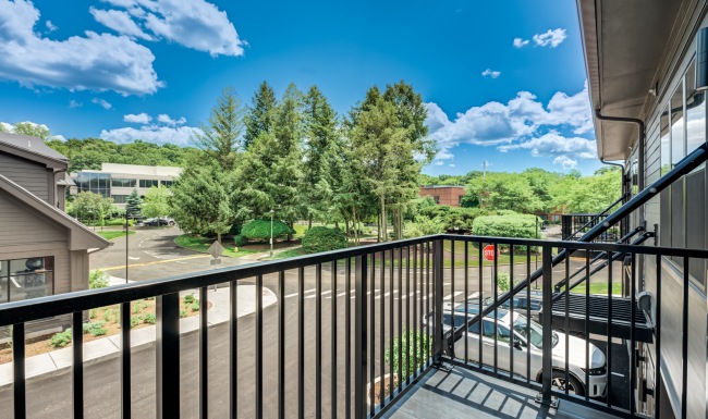 Scenic view of lush green trees and blue sky from a private apartment balcony with black railing at Brookside Wilton in CT